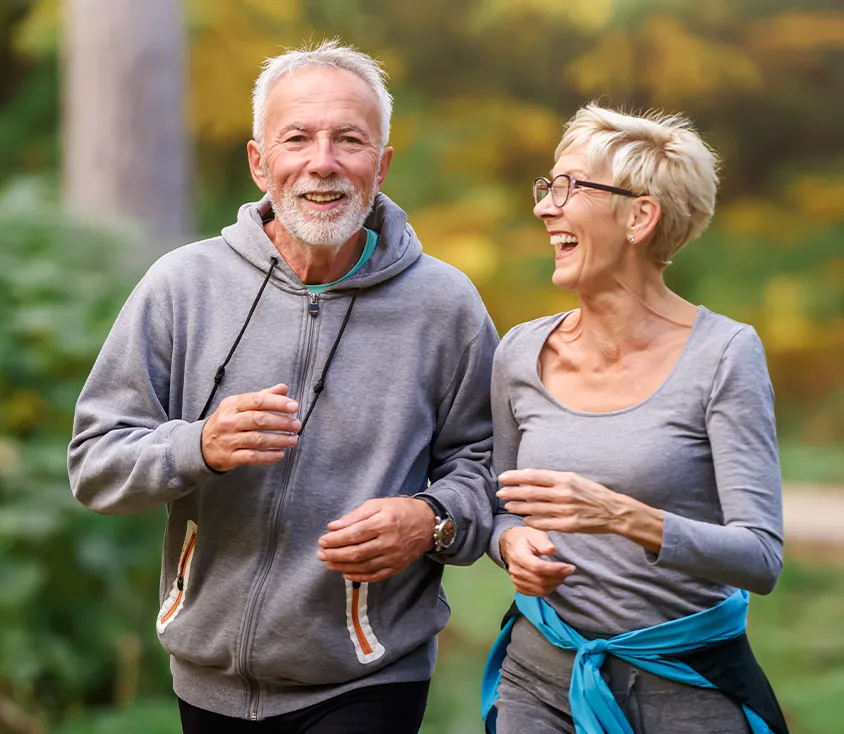 A smiling older couple in grey athletic wear jogging together outdoors