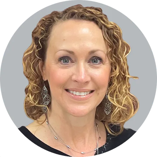 Portrait of Physical Therapist Carolyn S. Poston wearing a black top and drop earrings, smiling with a light gray background