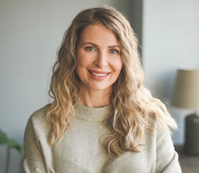 A smiling woman with long wavy blond hair in a light sweater