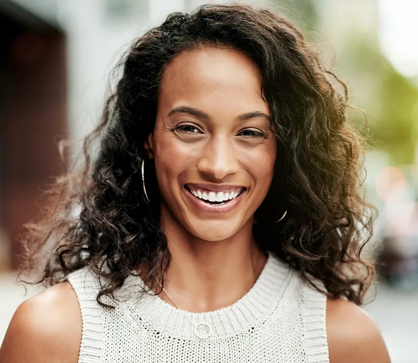 A smiling young woman with curly dark hair outdoors