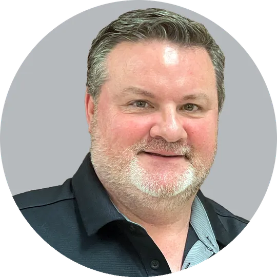 Portrait of Physical Therapist Assistant Warren McComas wearing a dark collared shirt, smiling with a light gray background