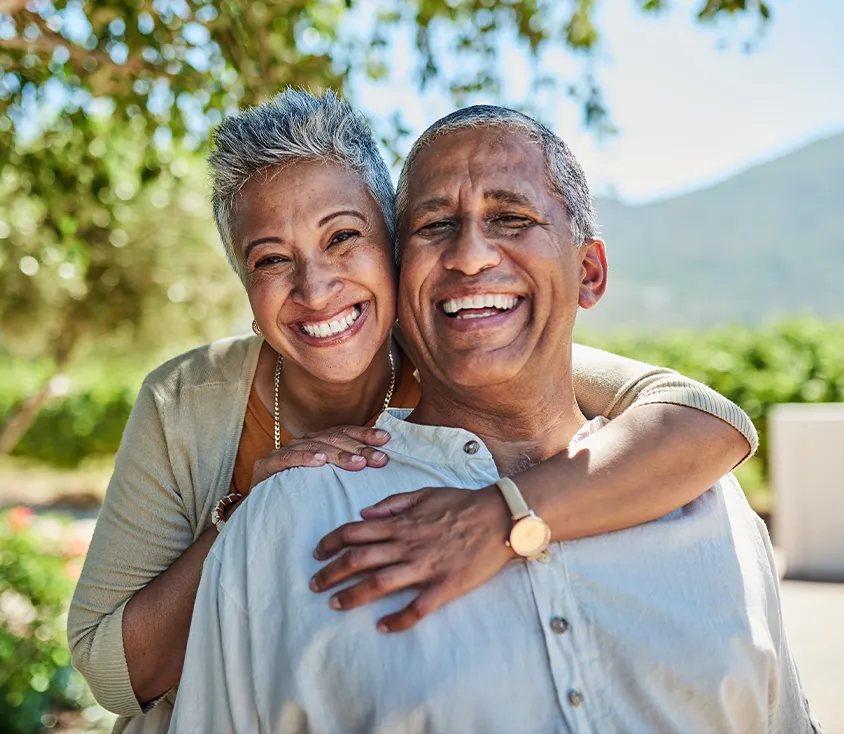 A smiling older couple embracing outdoors on a sunny day
