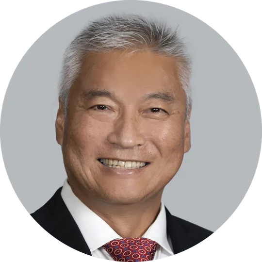 Portrait of Dr. Chris Kim wearing a blue suit, white shirt, and red patterned tie, smiling with a light gray background