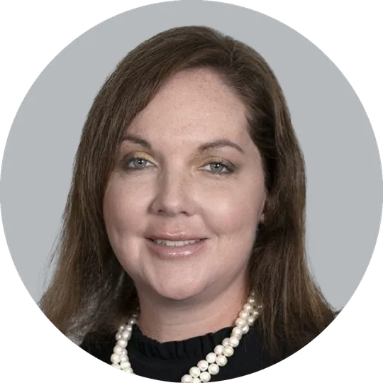 Portrait of Nurse Practitioner Tara Tackett wearing a black shirt, and a pearl necklace, smiling with a light gray background