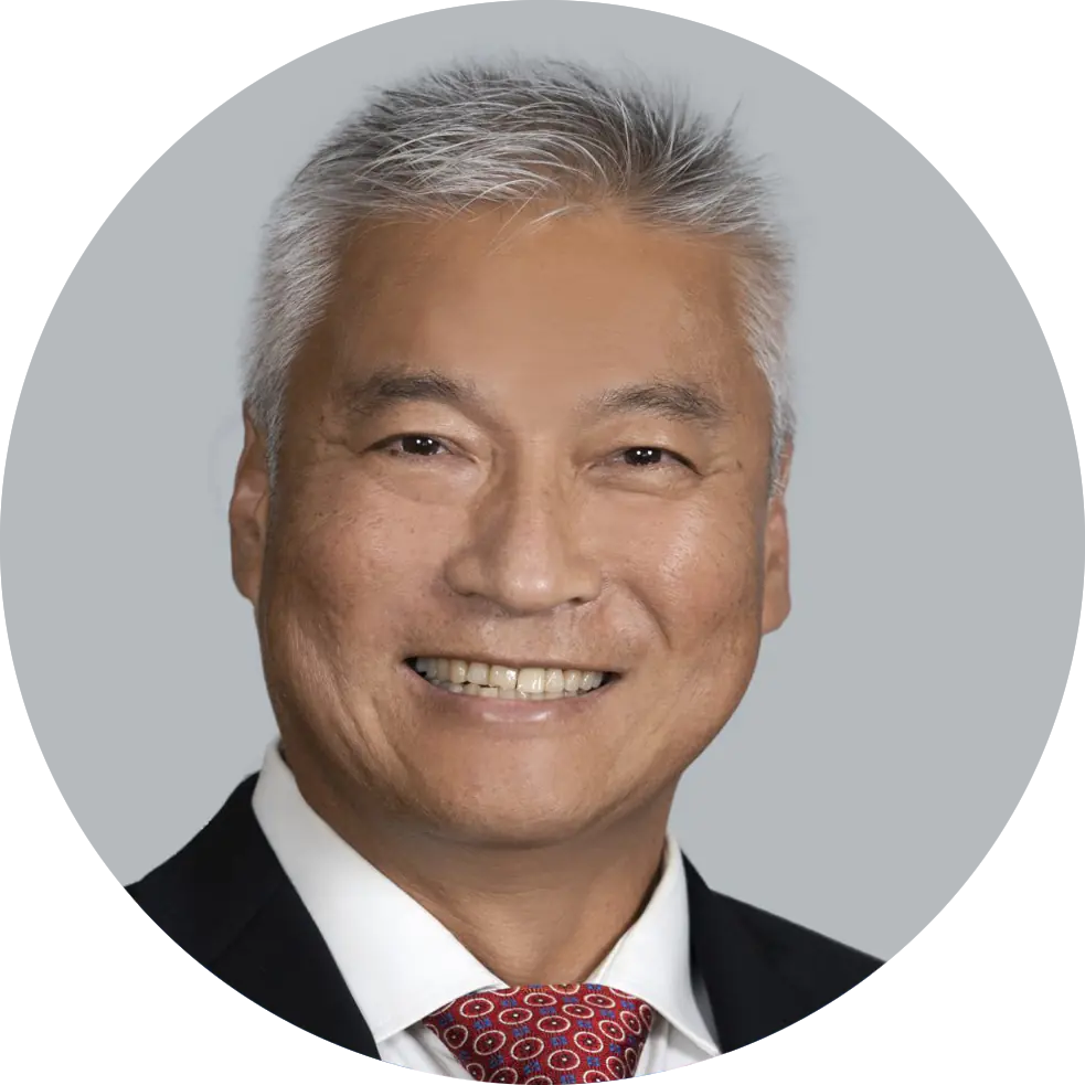 Portrait of Dr. Chris Kim wearing a blue suit, white shirt, and red patterned tie, smiling with a light gray background