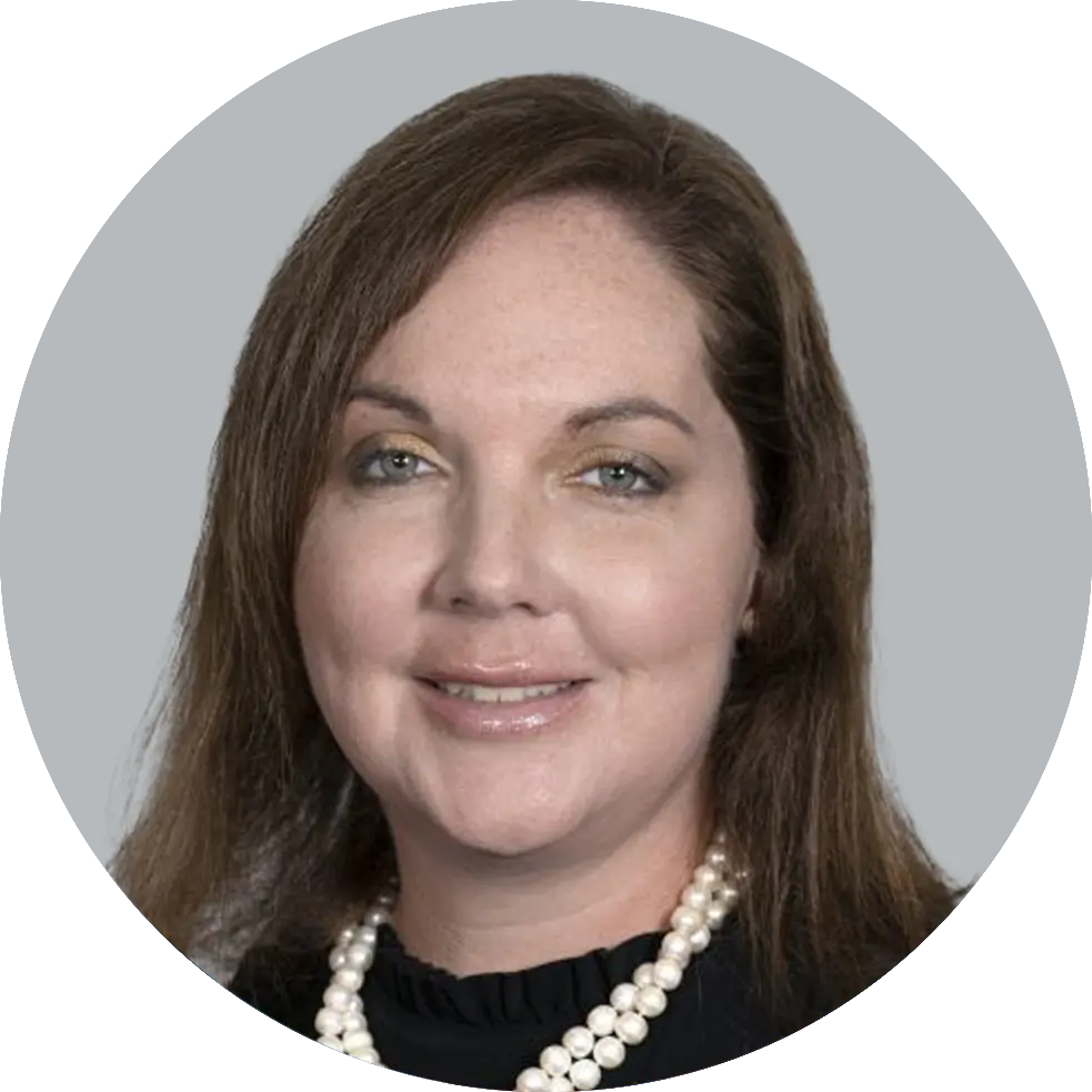 Portrait of Nurse Practitioner Tara Tackett wearing a black shirt, and a pearl necklace, smiling with a light gray background