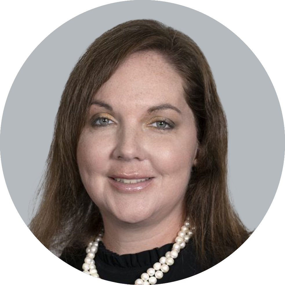 Portrait of Nurse Practitioner Tara Tackett wearing a black shirt, and a pearl necklace, smiling with a light gray background